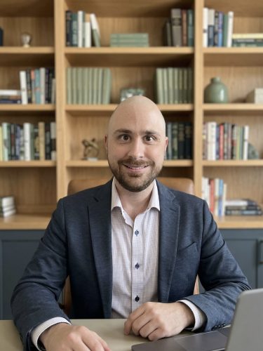 rofessional headshot of Dr. McWilliams, a board-certified psychiatrist in Columbia, MD. He is a smiling, bald man with a beard, wearing a navy blue blazer and a button-down shirt, set against a soft background. Dr. McWilliams provides personalized psychiatry services, medical management, and therapy for adults and adolescents in Columbia, Maryland, and surrounding areas. This photo reflects his compassionate approach to mental health care