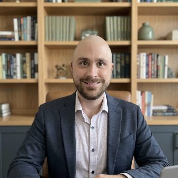 rofessional headshot of Dr. McWilliams, a board-certified psychiatrist in Columbia, MD. He is a smiling, bald man with a beard, wearing a navy blue blazer and a button-down shirt, set against a soft background. Dr. McWilliams provides personalized psychiatry services, medical management, and therapy for adults and adolescents in Columbia, Maryland, and surrounding areas. This photo reflects his compassionate approach to mental health care